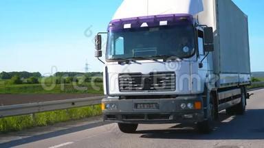 摄像机跟随卡车，货物拖车在公路上行驶，并在夏季运输货物。 卡车驶过